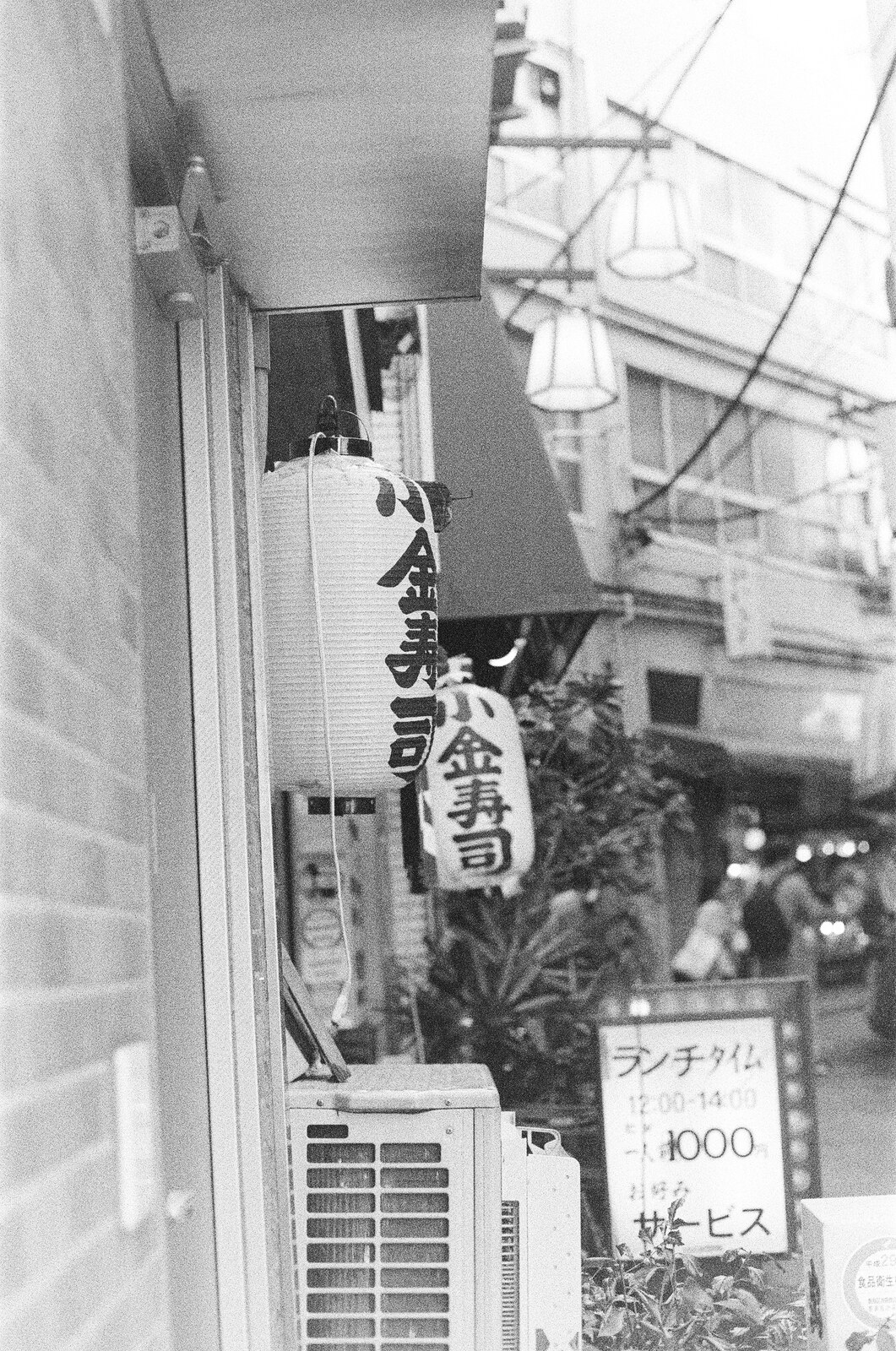 Lanternes japonaises suspendues devant une devanture, photo argentique noir et blanc