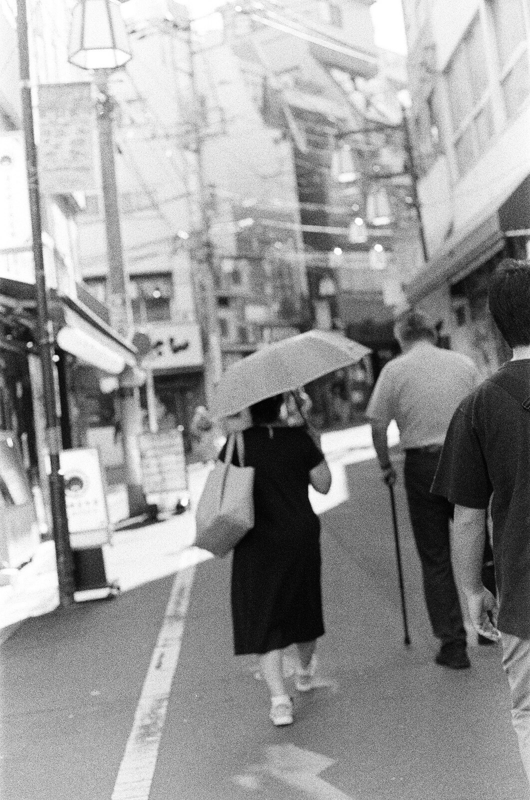 Passants sous un parapluie dans une ruelle japonaise, photo argentique noir et blanc