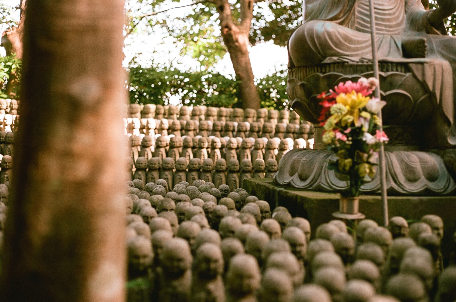 Statue de bodhisattva assise entourée de fleurs et de statuettes jizo